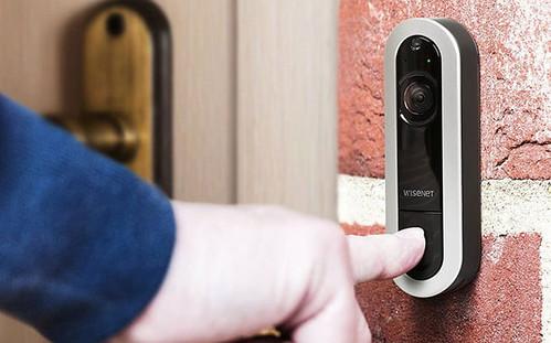 A person pressing a button on a doorbell with a security camera